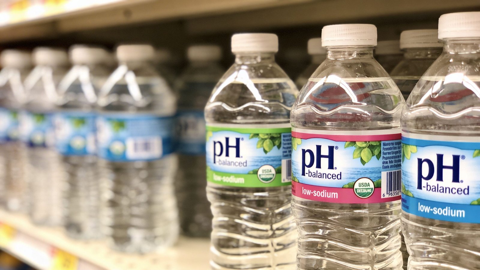 Several plastic bottles of pH-balanced, low-sodium drinking water arranged neatly on a supermarket shelf.